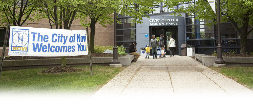 Residents approaching the entrance of City of Novi civic center with big outdoor lawn sign reading, "City of Novi Welcomes You"