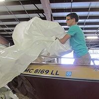 An individual standing in the front end of a stored boat with a bulky cover in their hands