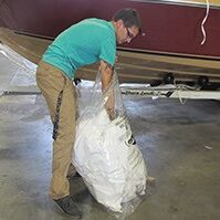 AN individual stuffing a white boat shrink-wrap cover in a Dr. Shrink receptacle bag